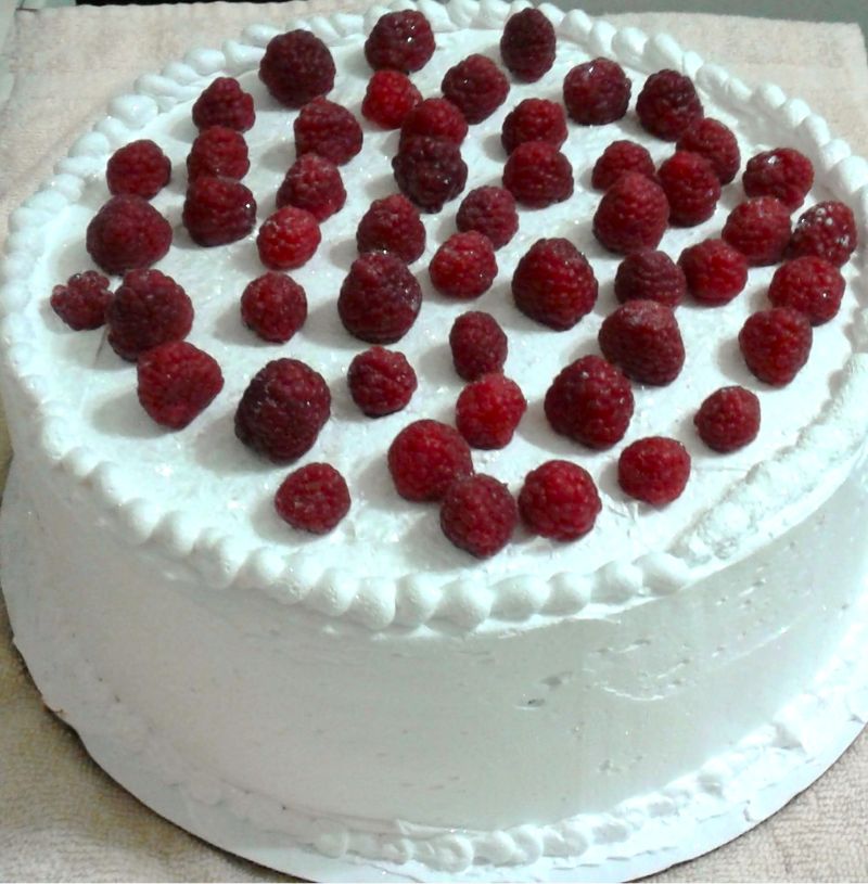 A raspberry cake topped with white frosting, edible glitter, and raspberries. 